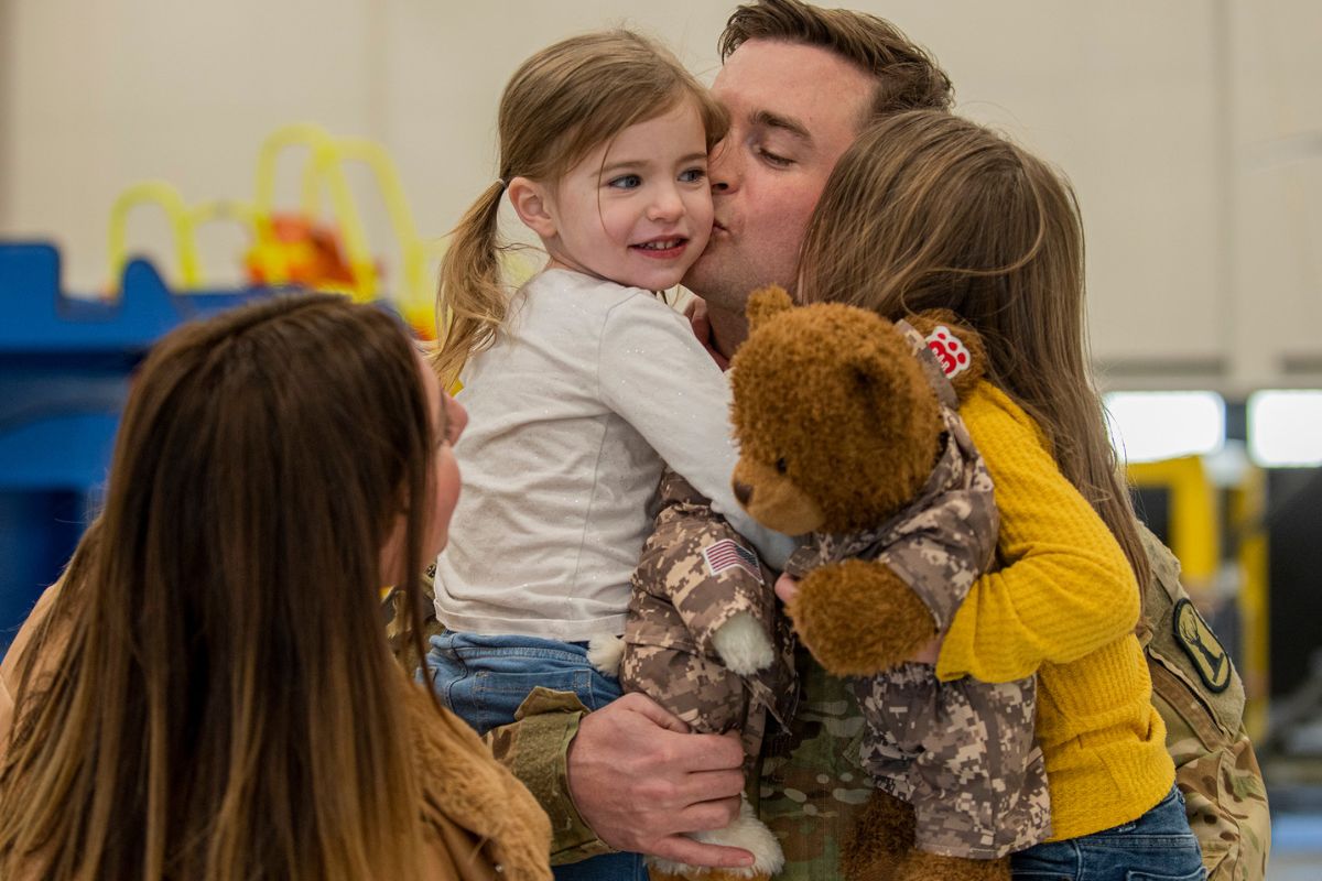 two children hug a service member